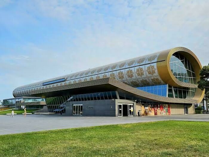 An exterior view of a modern building with unique, beautiful architecture resembling a rolled carpet.