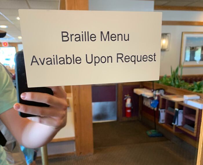 Sign on glass reads Braille menu available upon request, highlighting sarcastic irony in accessibility notices.