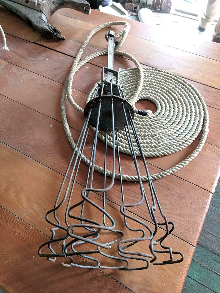 Old metal tool with multiple curved prongs laid on wooden table with coiled rope, part of internet solved mystery of unidentified objects.