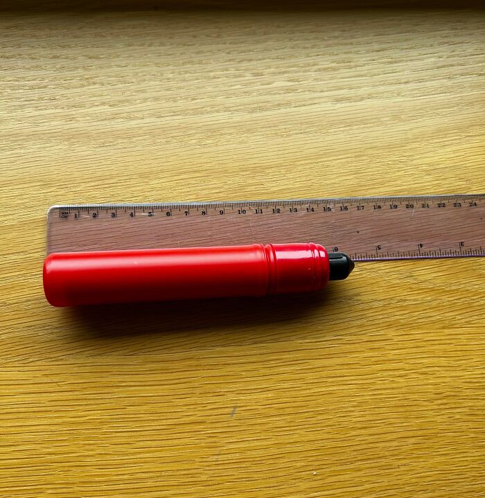 Red plastic object placed next to a ruler on a wooden surface, featured in internet mystery of unidentified objects solved.