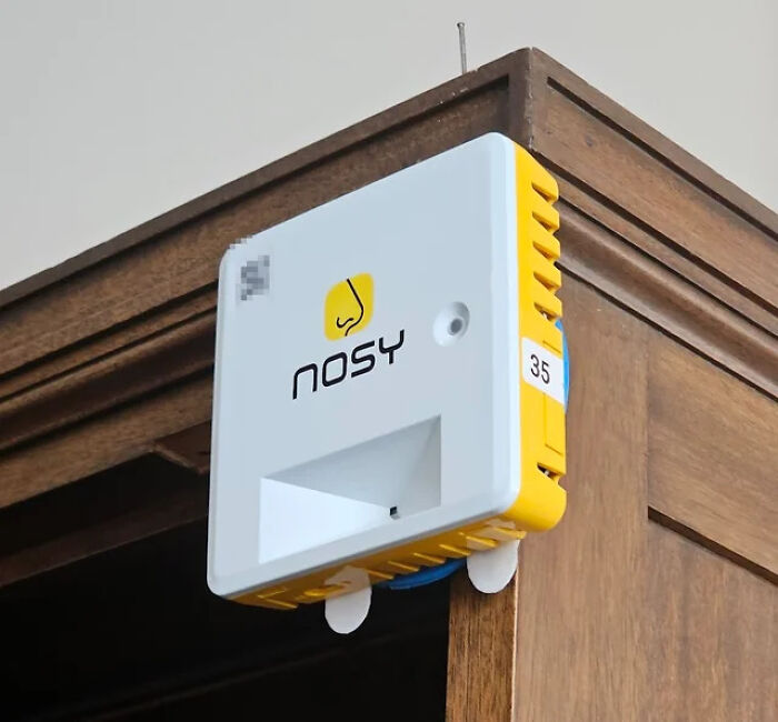 Small white and yellow device labeled Nosy mounted on a wooden surface, an example of unidentified objects solved by the internet.