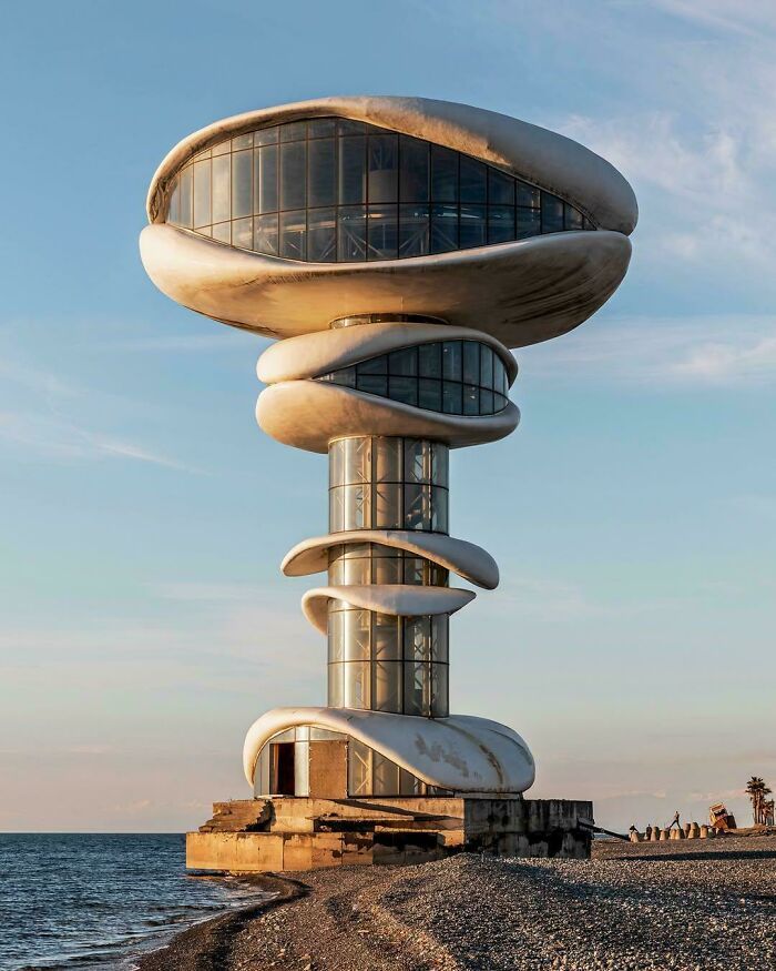 A futuristic, multi-tiered building with swirling concrete and glass, overlooking the sea, befitting an evil mastermind.