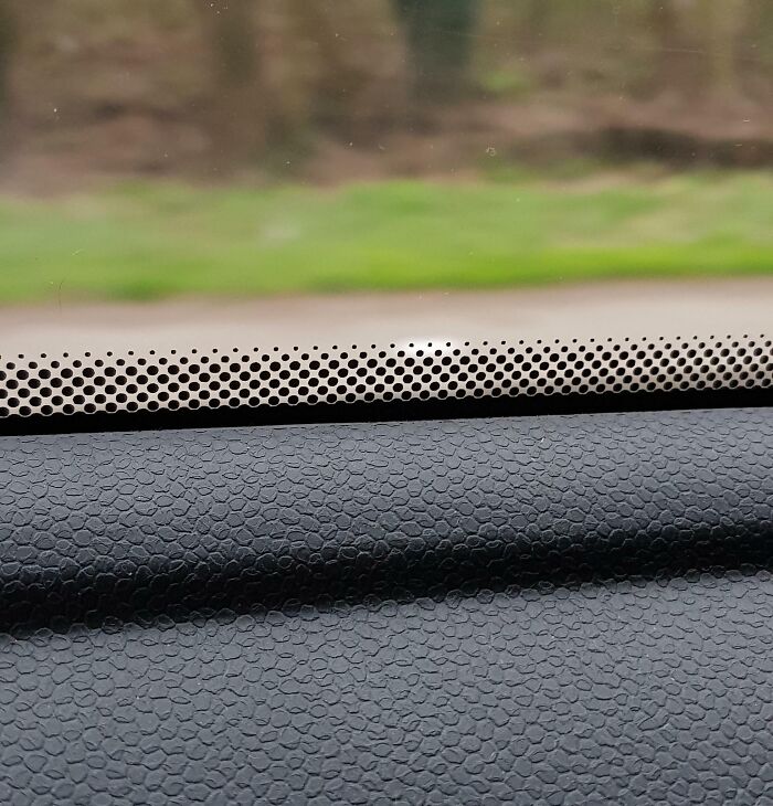 Close-up of a car dashboard and window with textured surface, featuring unidentified objects visible outside the vehicle.