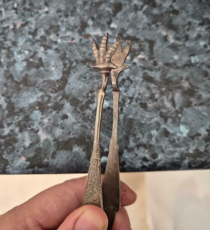 Hand holding two vintage metal utensils with unusual claw and fork-shaped ends, unidentified objects solved by the internet.