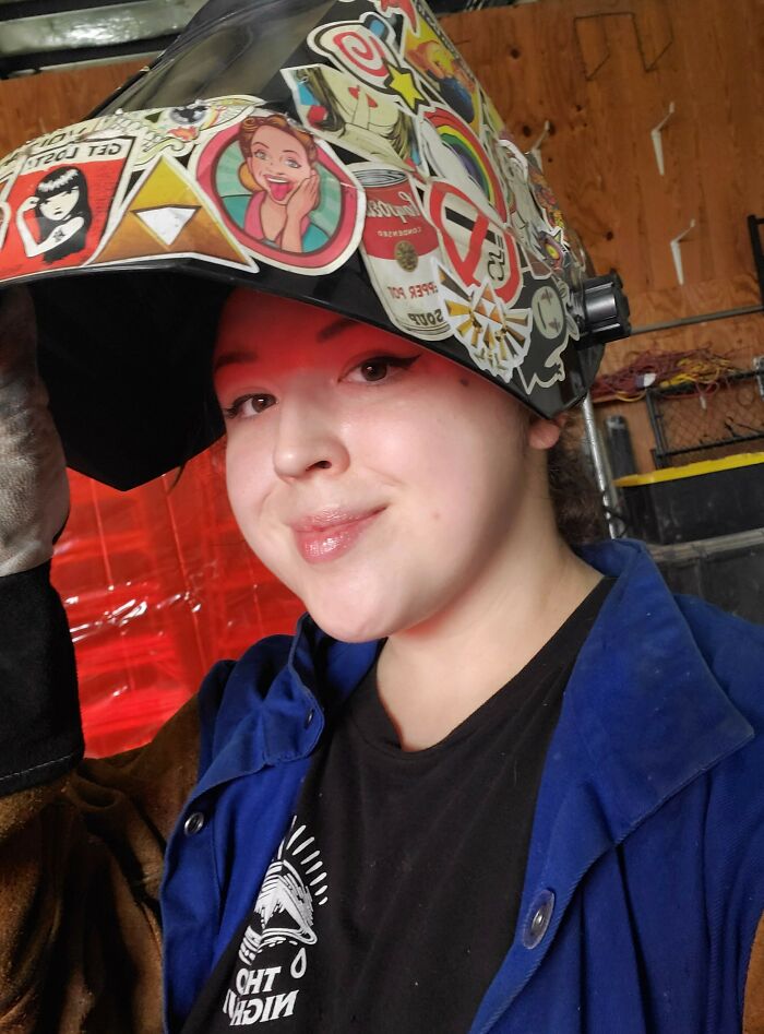 Young woman wearing a decorated welding helmet and protective coat, embracing power tools and lab coats over manicures.
