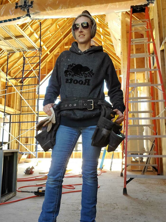 Woman wearing ear protection and tool belt in a construction site showcasing women using power tools and lab coats.
