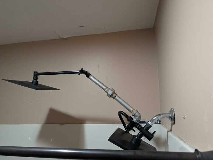 Improvised redneck engineering shower setup with mismatched pipes and showerheads mounted in a bathtub corner.