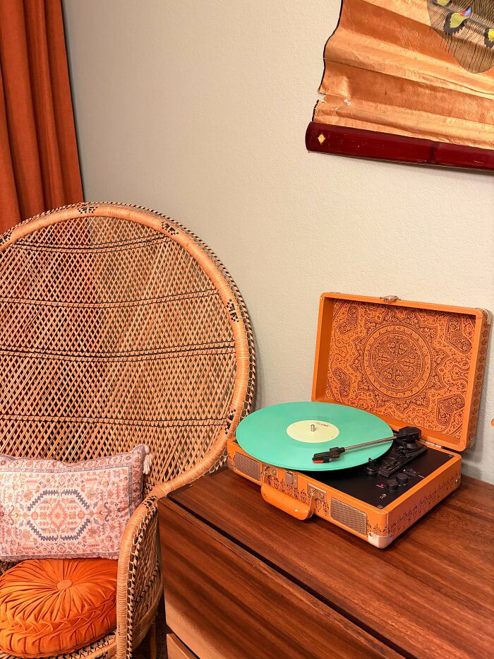 A vintage orange record player with a mint green record, a cool thrift store jackpot next to a wicker chair.
