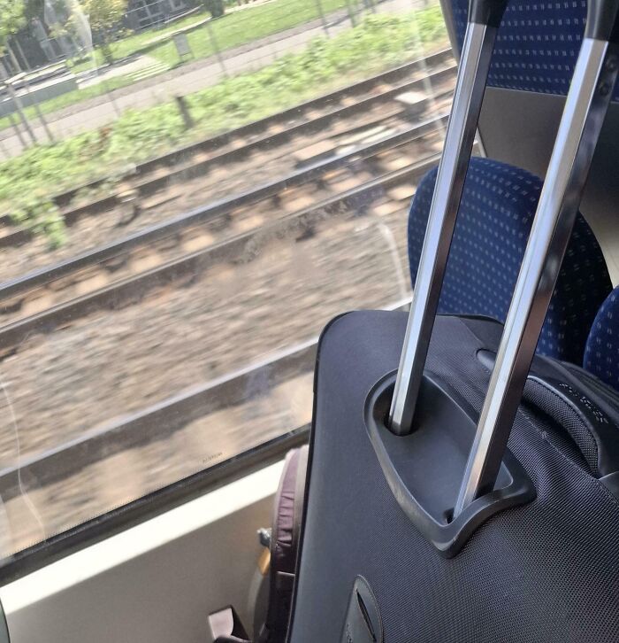 Suitcase with extended handle on a train seat next to a window showing railway tracks outside, illustrating tourist travel behavior.
