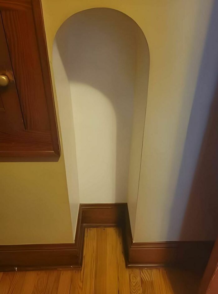 Narrow arched alcove in a home with wooden floor and brown baseboards, found in abandoned or forgotten homes.