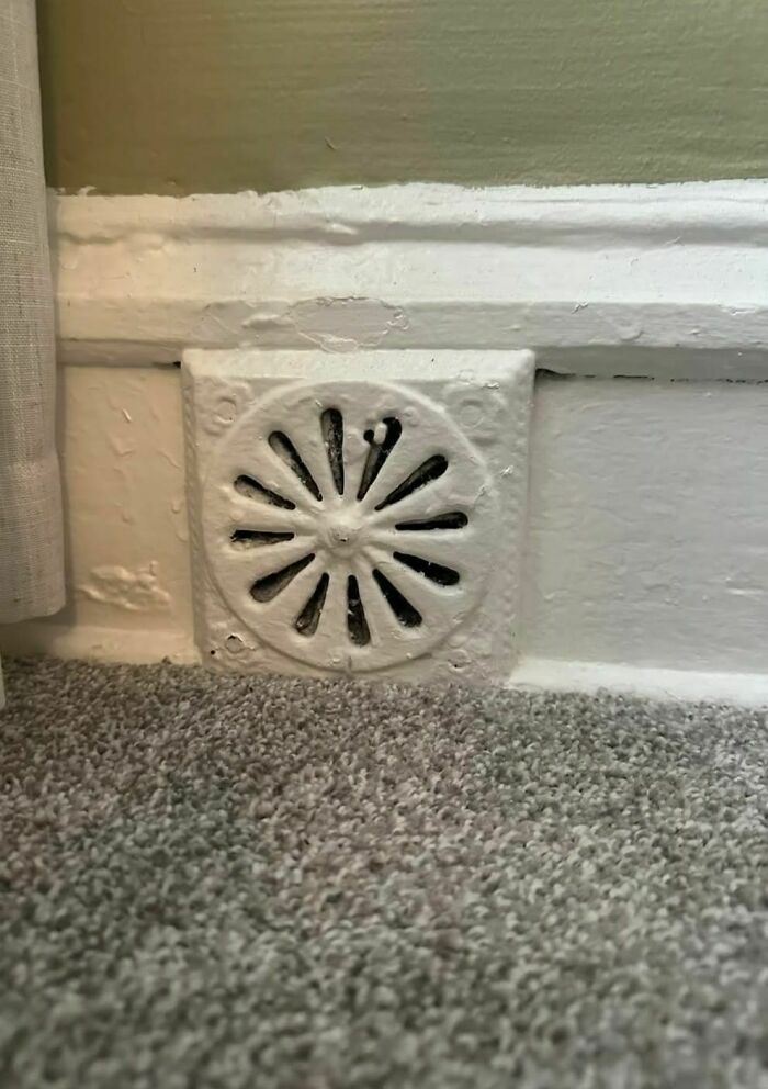 Old white painted vent cover on a baseboard in a carpeted room, a disturbing and weird thing found in homes abandoned.