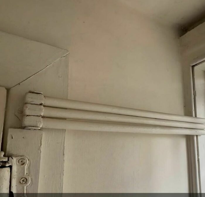 Three old, white heating pipes mounted on a wall in an abandoned or forgotten home interior.