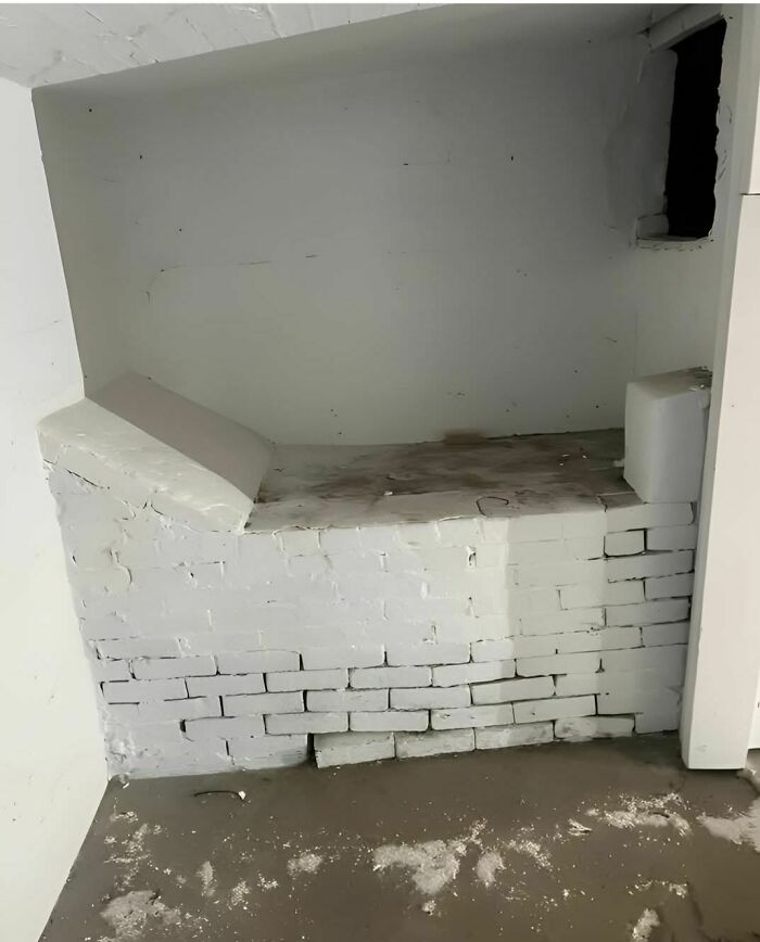 Abandoned home interior with strange, white-painted brick structure covered in dust and debris on the floor.