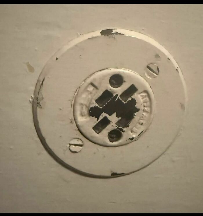 Old and worn electrical outlet cover found in a forgotten abandoned home showing chipped paint and rust.