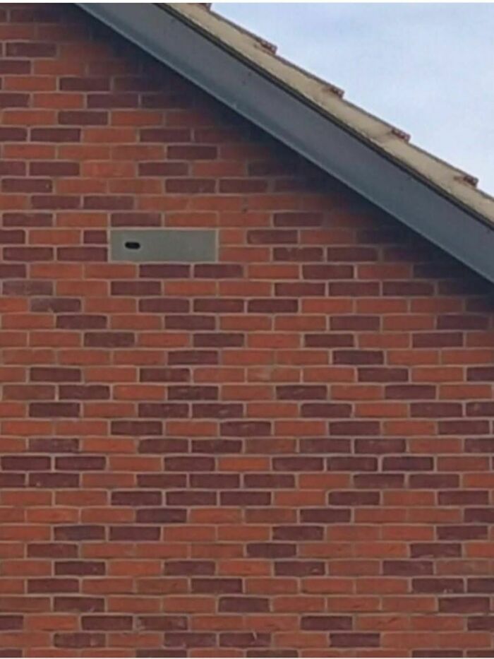 Brick wall of an abandoned or forgotten home with a sealed-up small window or ventilation opening visible near the roofline.