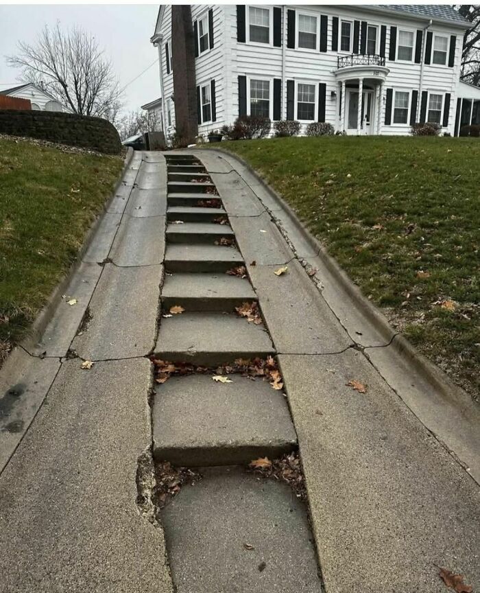 Concrete driveway with broken and uneven steps in front of an old abandoned or forgotten home outdoors
