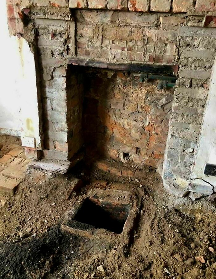 Exposed brick fireplace with dirt floor and a mysterious hole in an abandoned or forgotten home interior.