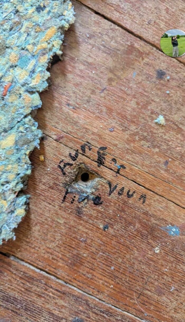 Close-up of old wooden floor with a small hole and strange handwritten text, found in an abandoned home.