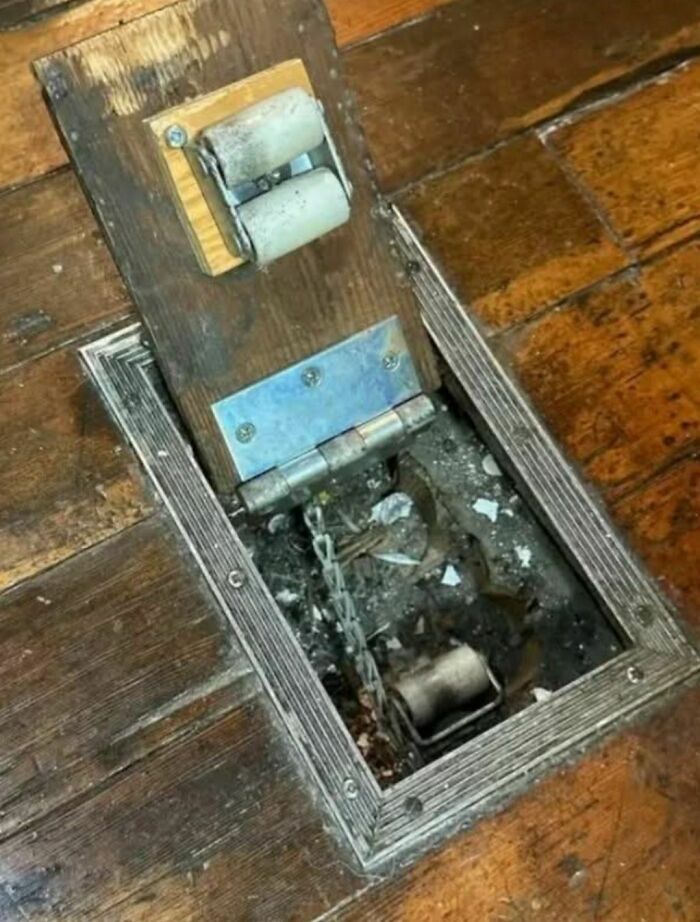 Old wooden floor panel lifted to reveal a hidden mechanism and chains in a disturbing abandoned home setting.