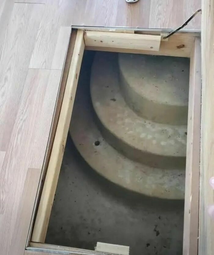 Hidden concrete spiral staircase beneath wooden floor in an abandoned or forgotten home with disturbing and weird features.