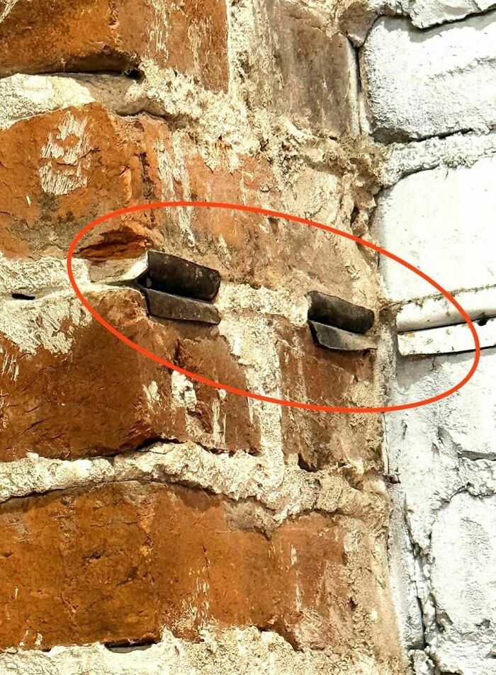 Rusty metal objects embedded in old brick wall, a disturbing and weird thing found in abandoned homes.