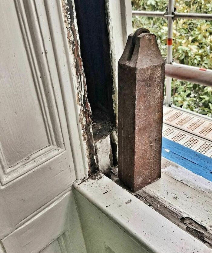 Rusty metal weight inside a decayed window frame, one of the disturbing and weird things found in abandoned homes.