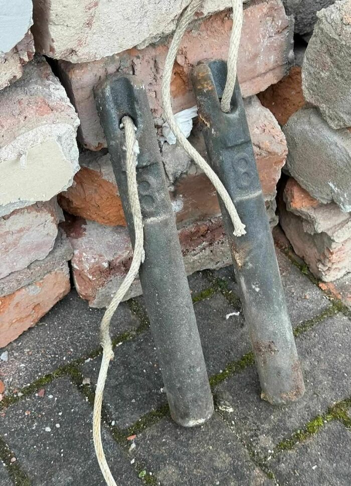 Two rusty metal rods with frayed ropes leaning against a c*****d brick wall in an abandoned home setting.