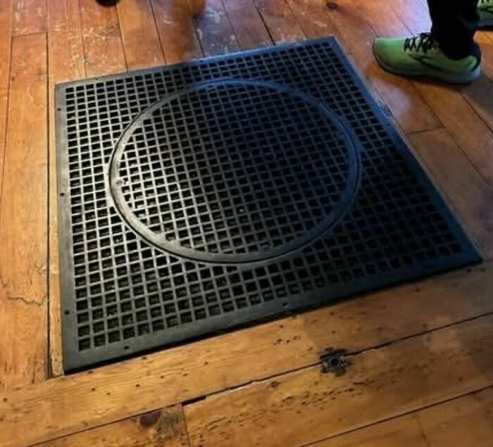 Black metal floor grate with a circular design found in an abandoned or forgotten home with wooden flooring nearby.