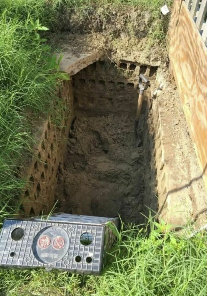 Deeply dug hole with dirt and old tools inside, viewed from above in a forgotten or abandoned home yard.