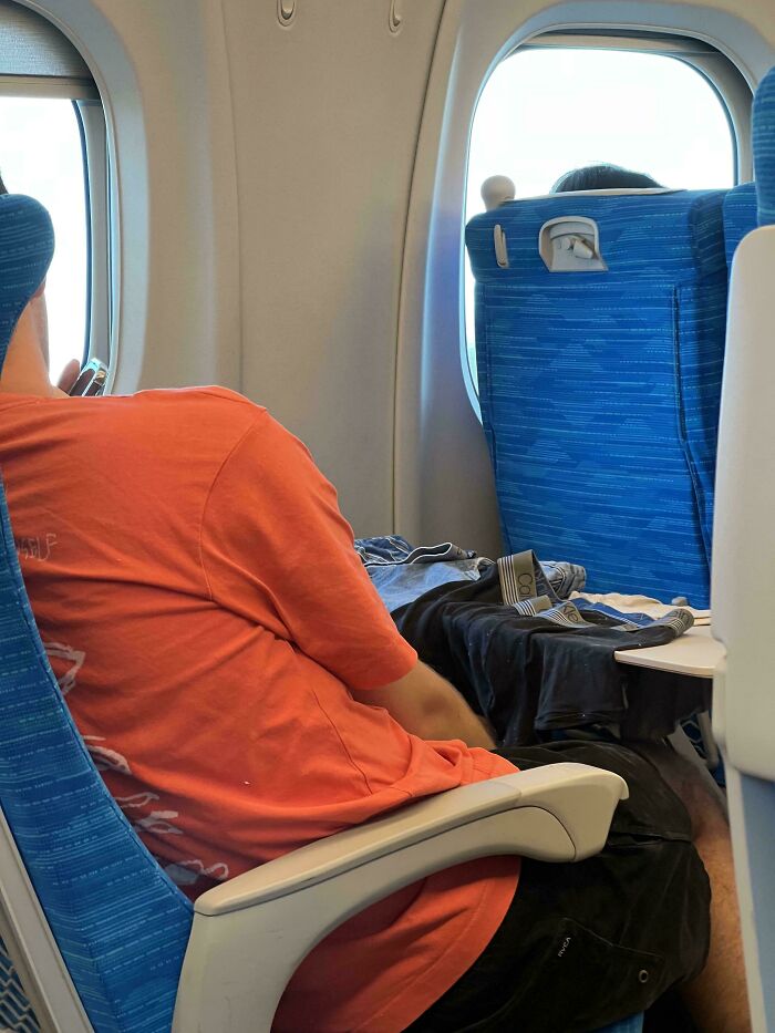 Tourist blocking airplane aisle with legs and clothes on seat, showing rude and entitled behavior while traveling.