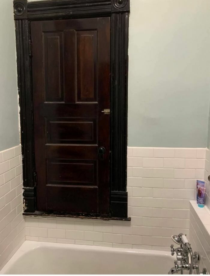 Old dark wooden door installed above bathtub in a bathroom showcasing disturbing and weird things found in abandoned homes.