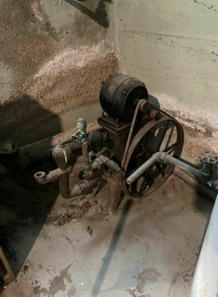 Old rusty machinery and pipes covered in dust in an abandoned home basement with damp concrete walls.