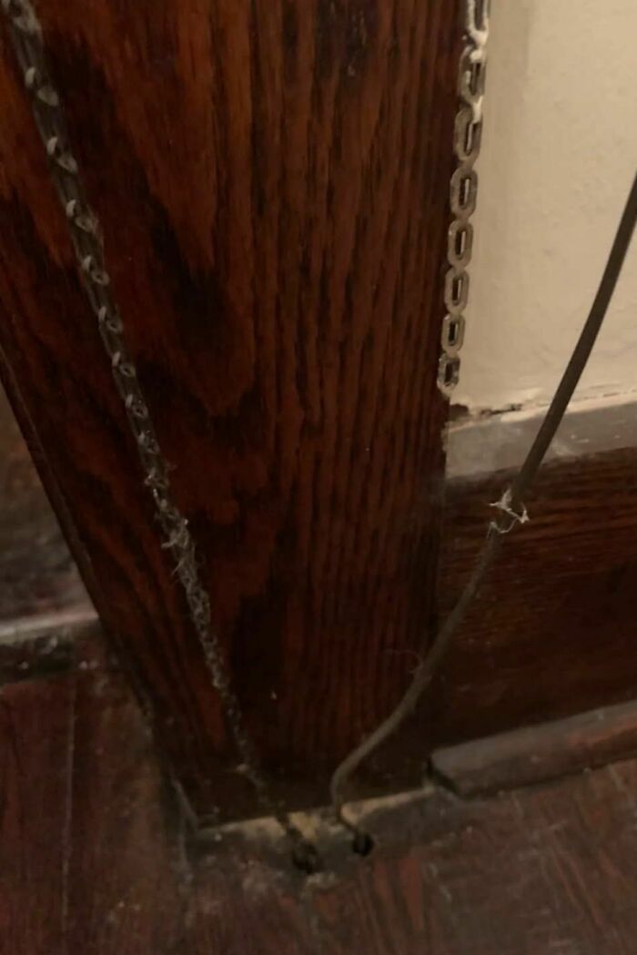 Worn chains and dusty wires hanging in a corner of an abandoned home with dark wood paneling and floorboards.