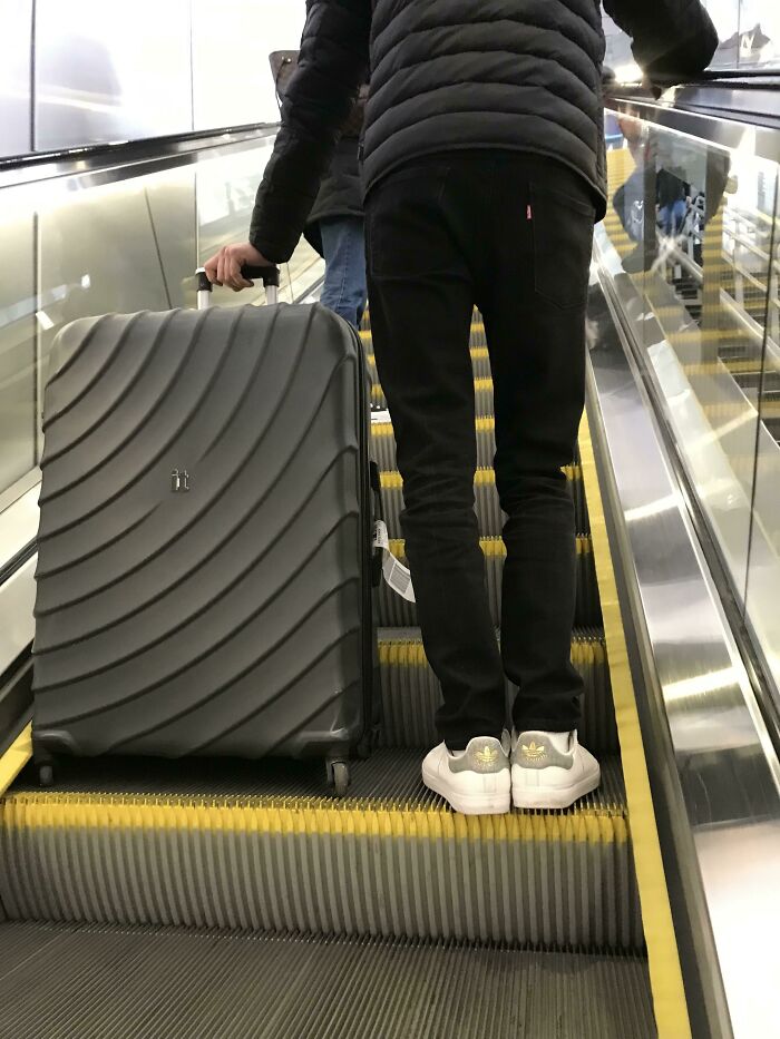 Tourist standing on escalator step with large suitcase, showing rude and entitled behavior in a public space.