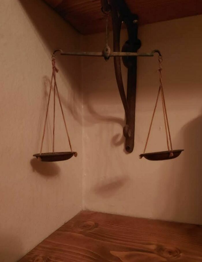 Rusty old hanging balance scale found in an abandoned home with wooden walls and ceiling corner.
