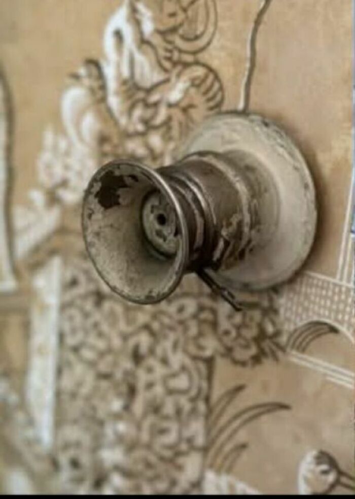 Rusty and damaged antique doorknob attached to wallpapered wall in an abandoned home setting.