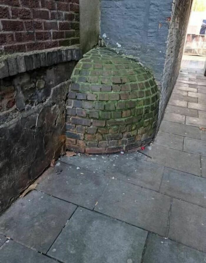 Moss-covered curved brick structure attached to old walls in a narrow abandoned alleyway with c*****d pavement.