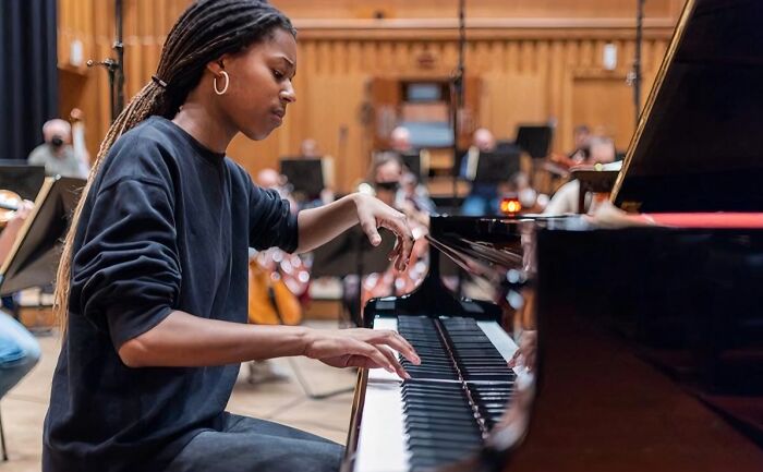 Young woman focused on playing grand piano during orchestral rehearsal, showcasing passion and skill in music performance.