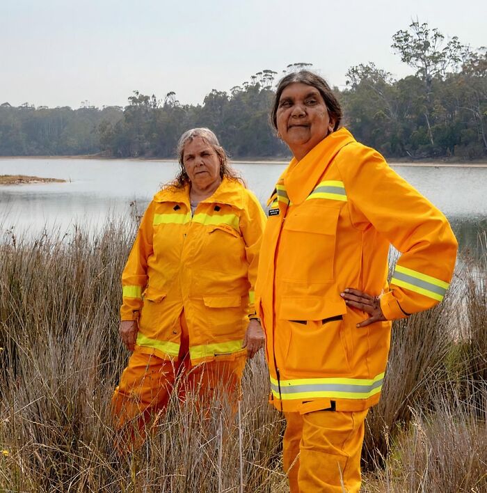 Two women in bright yellow protective clothing standing near a lake, representing women in power tools and lab coats fields.