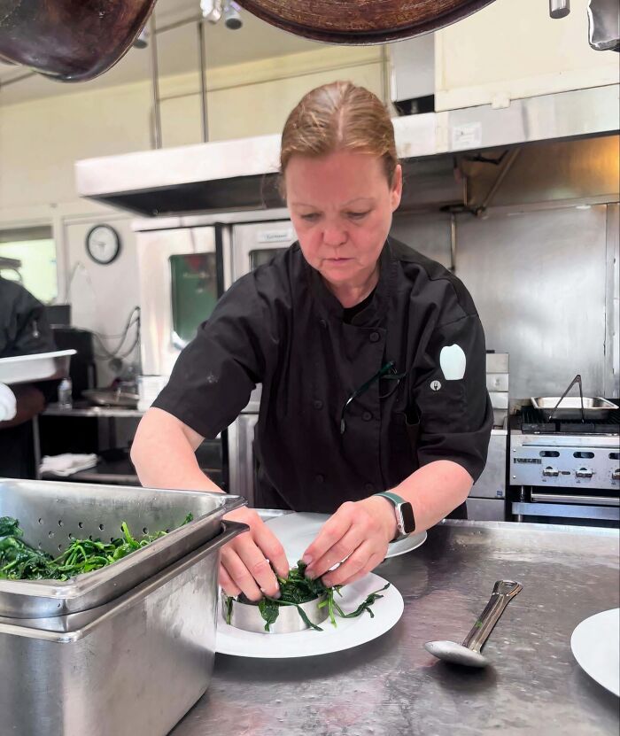 Woman in lab coat preparing food in a professional kitchen, showcasing power tools and lab coats over manicures.