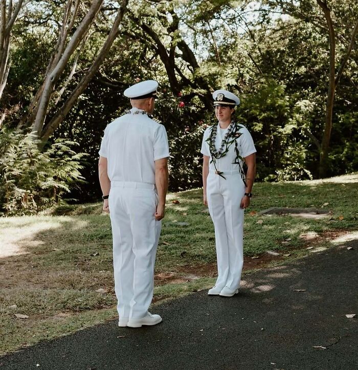 Two people in white naval uniforms standing outdoors surrounded by trees, representing women choosing power tools and lab coats.