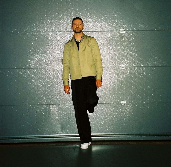 Man in casual outfit standing against textured wall under bright lighting, illustrating custom 2.5 million mobile mansion lifestyle.