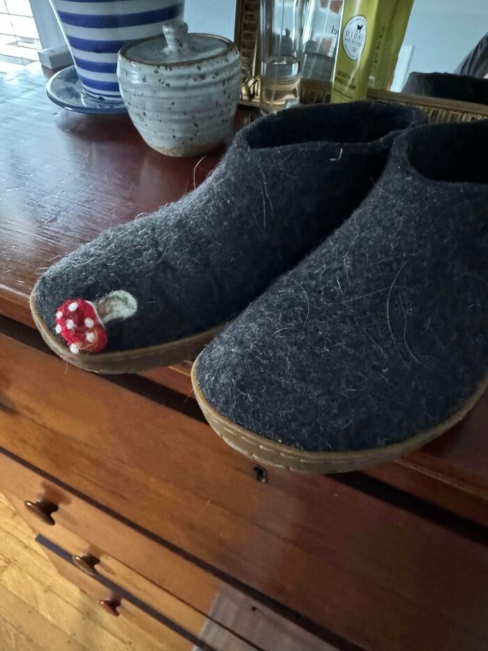 Dark gray felt slippers with a red and white mushroom embroidery on a wooden dresser. A Buy It For Life purchase.