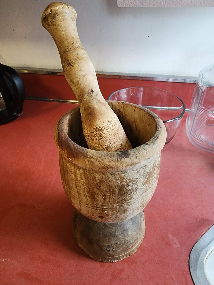 A rustic wooden mortar and pestle sits on a red countertop, showcasing a reliable Buy It For Life item.