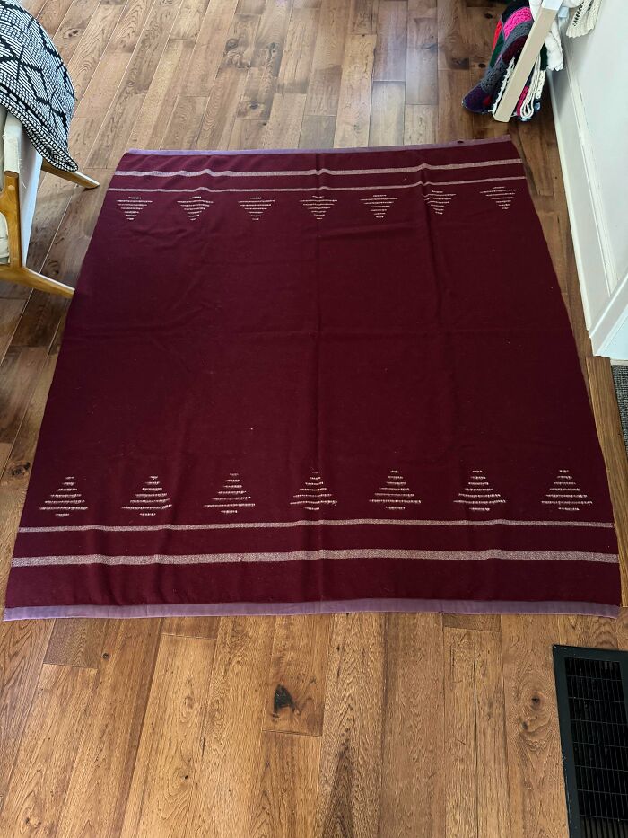 A dark red textile with light-colored horizontal stripes and triangle patterns on a wooden floor, a Buy It For Life purchase.