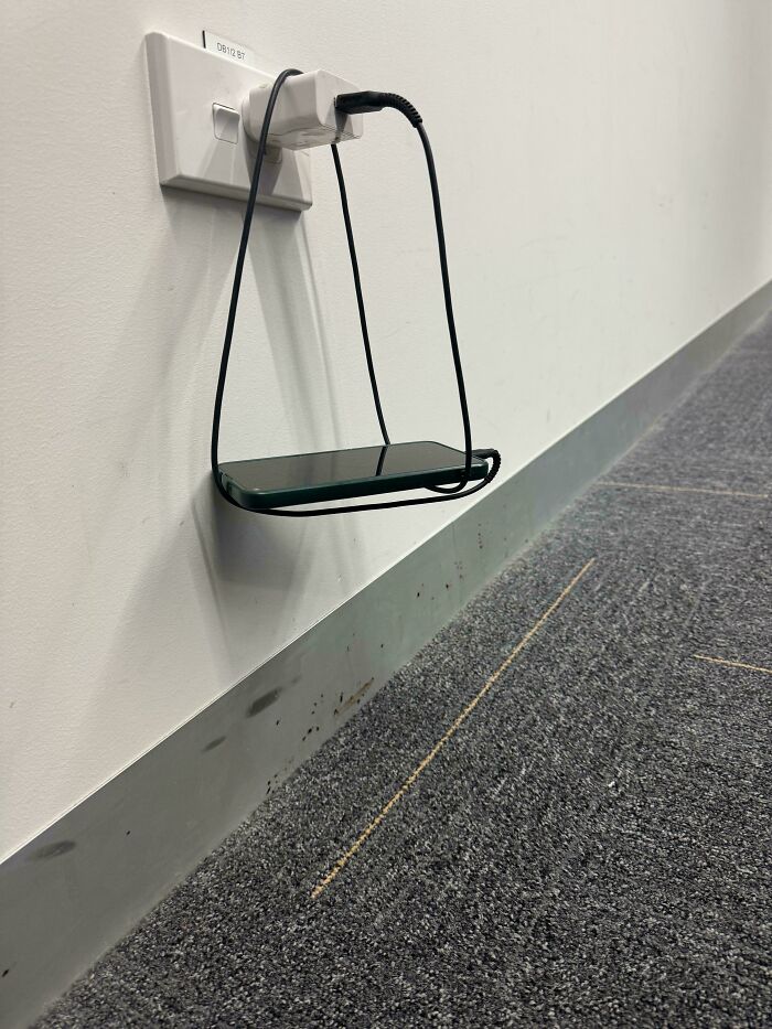 A mildly interesting picture of a phone charging from a wall outlet, suspended by its cable.