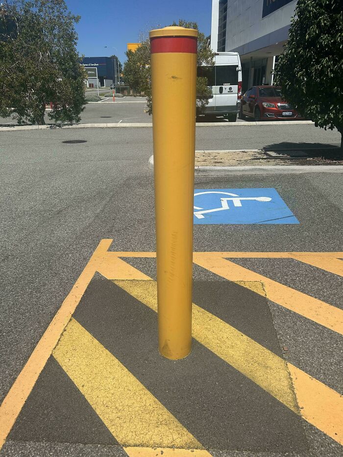 A mildly interesting picture of a yellow bollard on a parking lot with a handicapped spot.