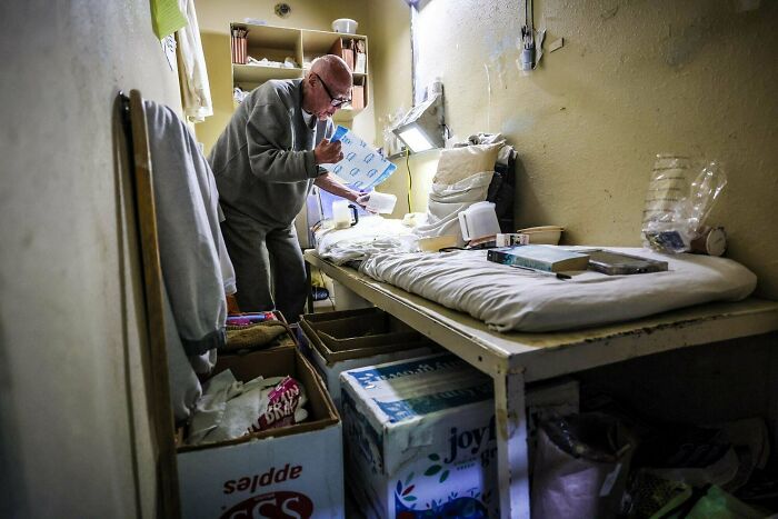 Elderly man in a sparse prison cell with basic belongings
