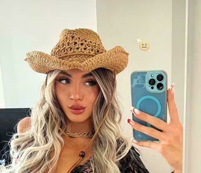 Woman wearing a straw hat taking a selfie with phone