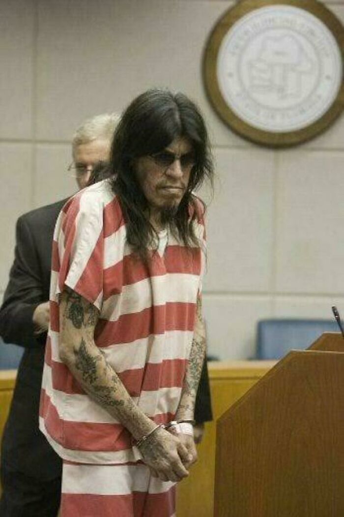 Prisoner in striped uniform with long hair and tattoos in courtroom